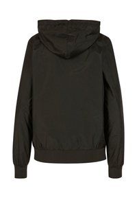 Black hooded jacket made of smooth, lightweight fabric. Features elastic cuffs and hem, with a simple, minimalist design. Back view.
