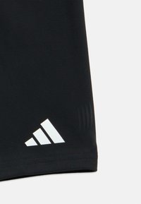 Μαύρο αθλητικό σορτς από ελαστικό ύφασμα. Διαθέτει λογότυπο με τρεις λευκές ρίγες και διακριτική υφή κατά μήκος του τελειώματος.