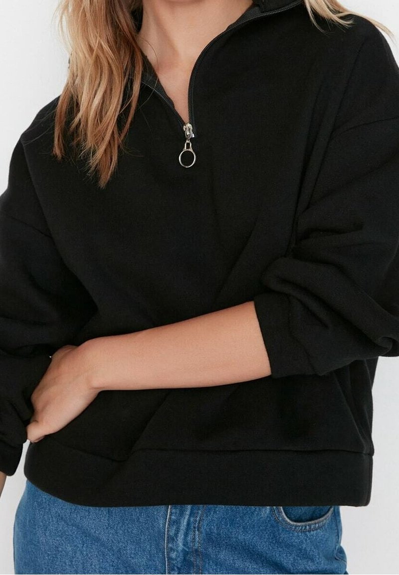 Sudadera negra de felpa con cuello con cremallera de cuarto, corte relajado, mangas con puños y tejido texturizado. Combinada con jeans de mezclilla azul.