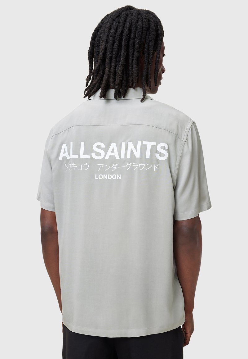 Szara koszulka krótki rękaw o luźnym kroju, z dużym białym napisem "ALLSAINTS LONDON" z tyłu. Gładka tekstura materiału.