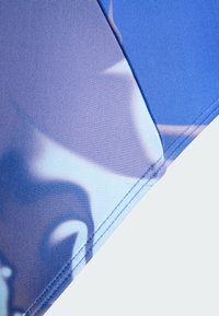Modrý elastický materiál s hladkou texturou a jemným abstraktním vzorem. Viditelné švy podél okrajů.