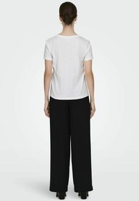 T-shirt blanc à manches courtes, coupe décontractée, associé à un pantalon large noir. Tissu lisse et design simple, sans motifs ni graphiques visibles.