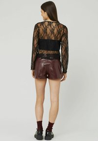 Haut à manches longues en dentelle noire avec un dos transparent, associé à un short en cuir verni bordeaux et à des chaussures noires à semelles épaisses. Chaussettes avec des accents rouges.