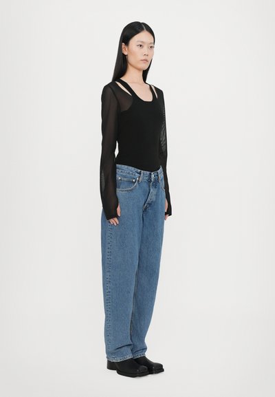 Μαύρο τοπ με μακριά μανίκια και διαφανή μανίκια, σε συνδυασμό με φαρδιά μπλε τζιν και μαύρες πλατφόρμες. Απλός, καθαρός σχεδιασμός.