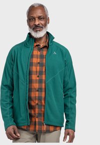 Grüne Fleecejacke mit einem Reißverschluss vorne, hohem Kragen und Seitentaschen, getragen über einem orange-schwarzen Karoshemd.