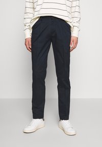 Granatowe, dopasowane spodnie wykonane z lekkiego materiału, z bocznymi kieszeniami, gładką teksturą i eleganckim krojem, zestawione z białymi sneakersami.