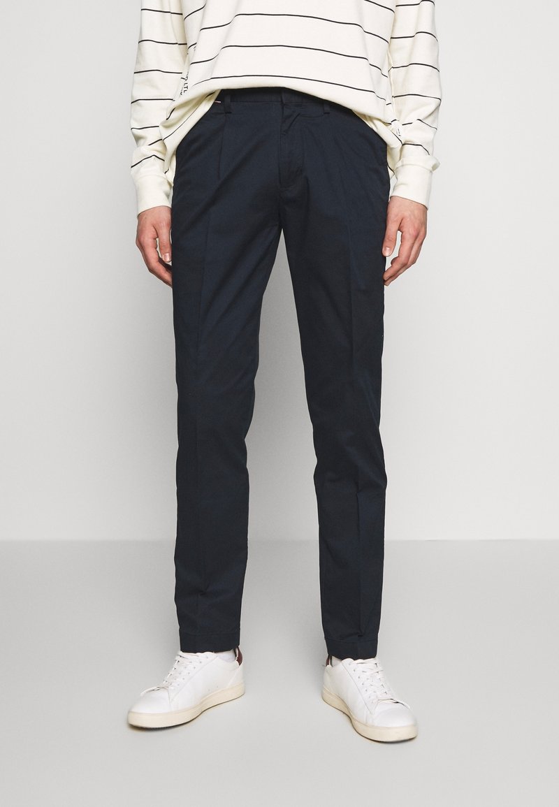 Granatowe, dopasowane spodnie wykonane z lekkiego materiału, z bocznymi kieszeniami, gładką teksturą i eleganckim krojem, zestawione z białymi sneakersami.