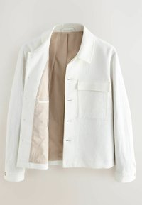 Giacca bianca in tessuto texturizzato, con collo a riviera, bottoni frontali e una tasca applicata sul lato sinistro. Fodera beige visibile.