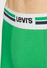 Πράσινα βαμβακερά σλιπ με λευκή ζώνη που διαθέτει μαύρες και πράσινες ρίγες και το λογότυπο "Levi's" σε μαύρο κείμενο.