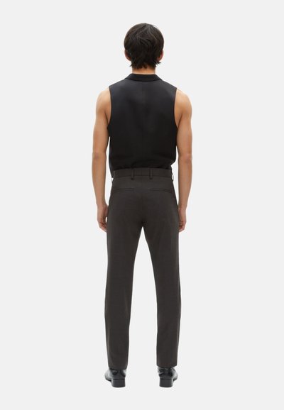 Schwarzes ärmelloses Oberteil kombiniert mit dunkelgrauen, maßgeschneiderten Hosen, die eine glatte Textur und eine schmale Passform aufweisen. Die Schuhe sind schwarz mit glänzender Oberfläche.