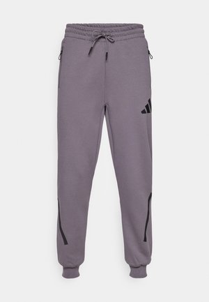 Grå joggebukser laget av mykt stoff, med snor i livet, glidelåslommer, svarte detaljer og en logo på venstre lår.