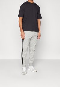 Šedé tepláky s černými bočními pruhy, které jsou kombinovány s černým tričkem s krátkým rukávem. Bílé sportovní boty dokončují outfit.