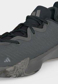 Gros plan d'une chaussure de sport grise et noire en tissu mesh, lacets noirs et semelle texturée avec un élément de design translucide.