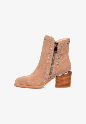 Stivale alla caviglia in suede beige con dettagli in metallo argentato, zip laterale e tacco in legno con base metallica.