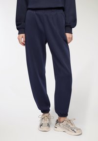 Pantaloni sportivi blu navy con vita e polsini elasticizzati, caratterizzati da una vestibilità ampia e una consistenza morbida. Abbinati a sneakers beige.