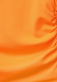 Oranje stof met een gladde textuur en geplooide details. Het materiaal lijkt rekbaar en lichtgewicht, geschikt voor casual kleding.