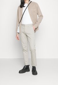 Beige knäppskjorta över en vit t-shirt, tillsammans med ljusbeige byxor och svarta chunky-skor. Minimalistisk svart axelremsväska.