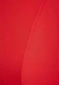 Tejido rojo con una textura suave y un panel acanalado en contraste. Los detalles de costura son visibles a lo largo de la costura para añadir interés al diseño.