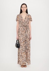 Abito maxi floreale beige, con maniche corte, design avvolgente, vita con cravatta e spacco frontale. Abbinato a una piccola borsa nera.