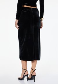 Sort fløjl midi-nederdel med en lige silhuet, der har en bageste lynlås, blød tekstur og syet kant. Bæres med sorte strophæle.