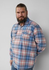 Jasnoniebieska koszula w kratę z guzikami, z czerwonymi i kremowymi akcentami, dwoma kieszeniami na piersi oraz długimi rękawami. Tkanina wygląda na miękką i lekko teksturowaną.