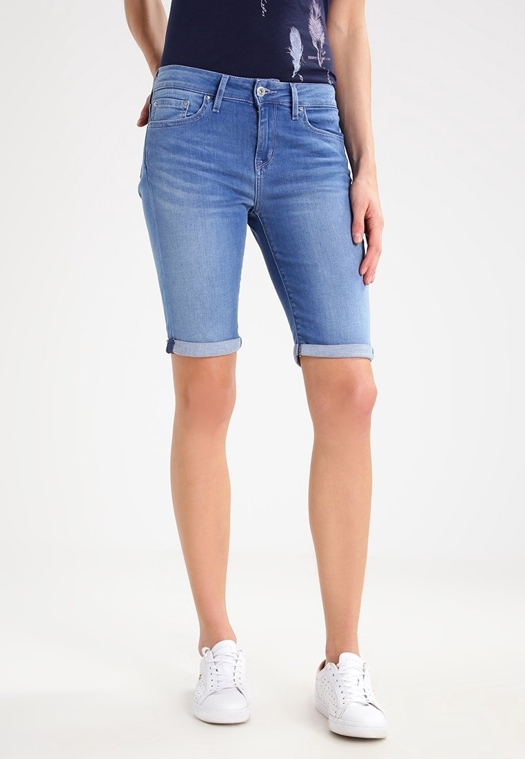 Ljusblå denimshorts med uppvikta fållar, en smal passform och framfickor. Matchade med vita sneakers och en mörk topp med ett fjädermönster.