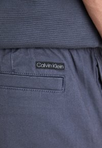 Calvin Klein marinebukser med en teksturert midjebånd og en baklomme med et svart logo-patch. Materialet ser jevnt og slitesterkt ut.