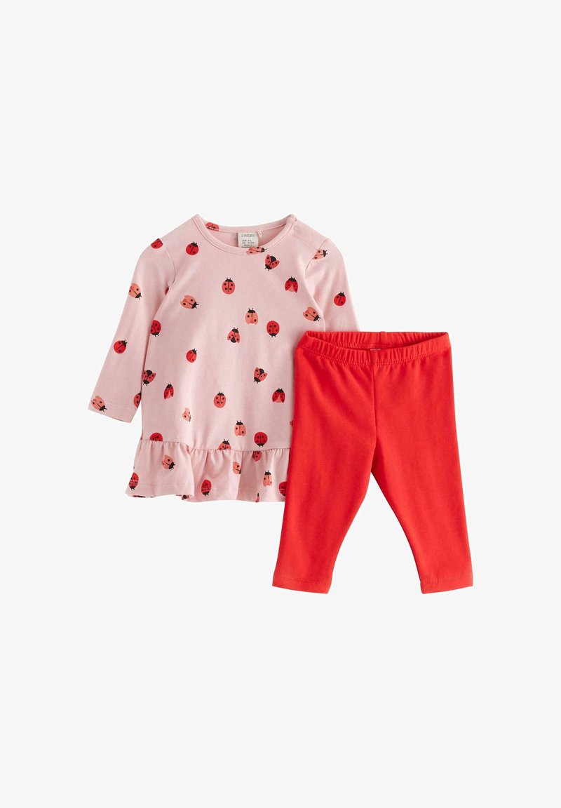 Rózsaszín, hosszú ujjú felső, katica mintával és fodros szegéllyel, egyszerű piros leggings-szel párosítva. Mindkét darab puha anyagból készült.