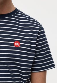 Marineblå og hvite stripe t-skjorte laget av bomull, med rund hals og en rød brodert logo på venstre brystområde.
