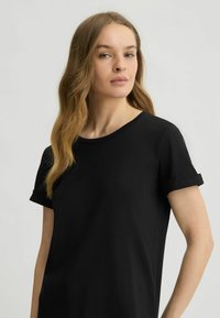 T-shirt nero a maniche corte con scollatura rotonda. Presenta orli arrotolati e un tessuto morbido e liscio con dettagli sottili all'orlo.