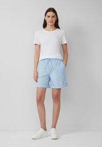 T-shirt blanche à manches courtes avec un imprimé de banane jaune, associé à un short bleu clair, longueur genoux, avec une ceinture élastique et des poignets.