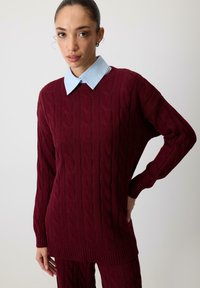 Burgundi värvi kudumisel väljakutsuv soe särk, millel on kaelus sinises toonis. Üks suurus sobivus sisaldab pikki varrukaid ning soonikkoes mansette ja allserva.