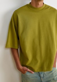 Olivgrön oversized t-shirt med hög krage och korta ärmar, tillverkad av smidig tyg. Har en rak skärning och minimala sömdetaljer.