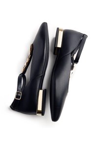 Scarpe in pelle nera con punta affusolata, cinturino alla caviglia e dettaglio dorato sul tallone. Texture liscia e design elegante.