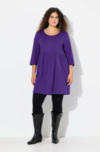 Lilla, knælang kjole med trekvart�ærmer og samlet talje, parret med sorte leggings og høje sorte støvler. Glat tekstur.