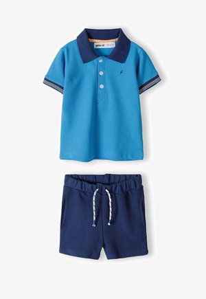Niebieska koszulka polo z granatowym kołnierzykiem i paskowanymi rękawami, zestawiona z granatowymi szortami z elastycznym pasem i sznurkiem.