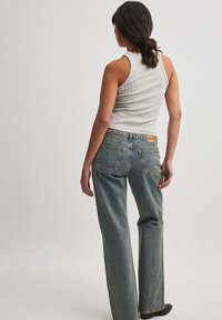 Top de tirantes acanalado gris combinado con unos vaqueros de cintura alta, de corte recto y textura de denim premium en un tono azul claro; se muestra vista posterior.
