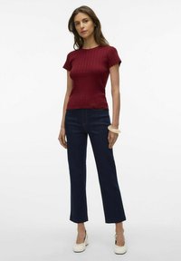 Haut en tricot côtelé bordeaux à manches courtes et ourlet festonné, associé à un pantalon en denim foncé évasé et des chaussures à talons blanches.