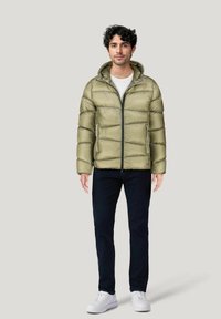 Giacca imbottita verde oliva con zip frontale, cappuccio e finitura texture, abbinata a pantaloni scuri e sneaker bianche. Design minimalista.