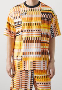 Lyhythemmatuinen, oranssi ja valkoinen kuviollinen T-paita, joka on valmistettu kevyestä kankaasta. Paidassa on rohkeita geometrisiä kuvioita ja musta ribbikaulus.