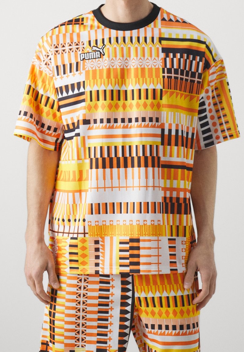 Lyhythemmatuinen, oranssi ja valkoinen kuviollinen T-paita, joka on valmistettu kevyestä kankaasta. Paidassa on rohkeita geometrisiä kuvioita ja musta ribbikaulus.