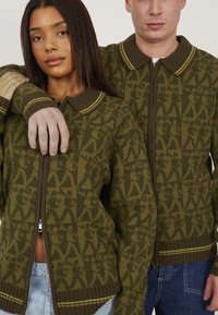 Green patterned zip-up sweaters with contrasting collar and hem accents. Material appears soft; includes a mix of geometric and organic motifs.