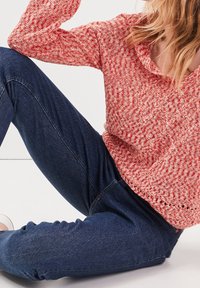 Czerwono-biały sweter o fakturze dzianiny z szerokim dekoltem, zestawiony z ciemnoniebieskimi dżinsami denim. Dżinsy mają klasyczny krój i subtelne detale szwów.