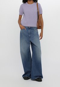 T-shirt lilla a coste con maniche corte, abbinata a jeans svasati blu sbiaditi. Una borsa a tracolla marrone e scarpe chunky nere completano l'outfit.