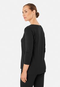 Czarna bluzka z długim rękawem, okrągłym dekoltem, miękką teksturą i luźnym krojem; ma delikatne detale w postaci szwów oraz zaokrąglony dół.