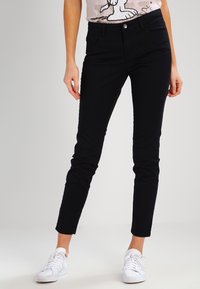 Černé elastické džíny, slim fit, s předním zapínáním na knoflík, pěti kapsami, hladkým povrchem a minimálním zdobením. V kombinaci s bílými teniskami.