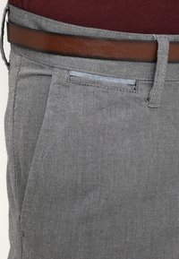 Pantalons tissés gris avec deux poches latérales, une ceinture en cuir marron et un détail de taille bleu clair contrastant.