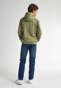 Felpa verde con tasca a marsupio, abbinata a jeans blu. La felpa presenta un cappuccio con coulisse e polsini a coste. Sneakers bianche.