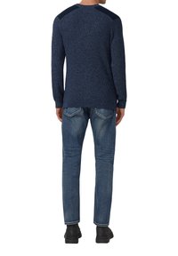Marineblauer Strickpullover mit strukturiertem Stoff, geripptem Halsauschnitt und Schulterdetails, kombiniert mit hellblauen Jeans und schwarzen Schuhen.