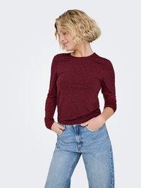 Chemise bordeaux à manches longues avec pois blancs, coupe ajustée, encolure ronde et tissu doux, associée à un jean taille haute bleu clair.